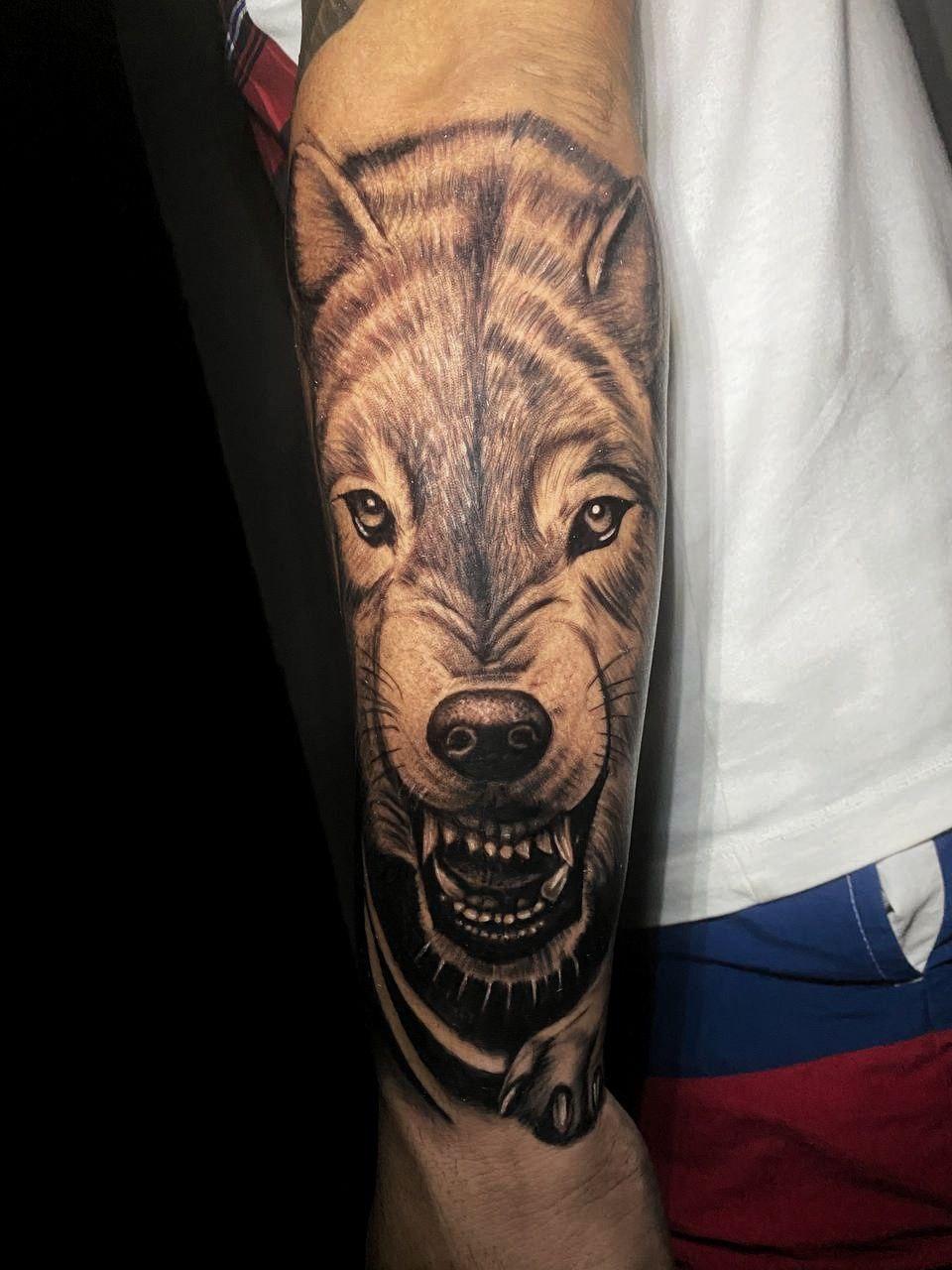 Tatuaje realista de lobo con expresión feroz en el brazo