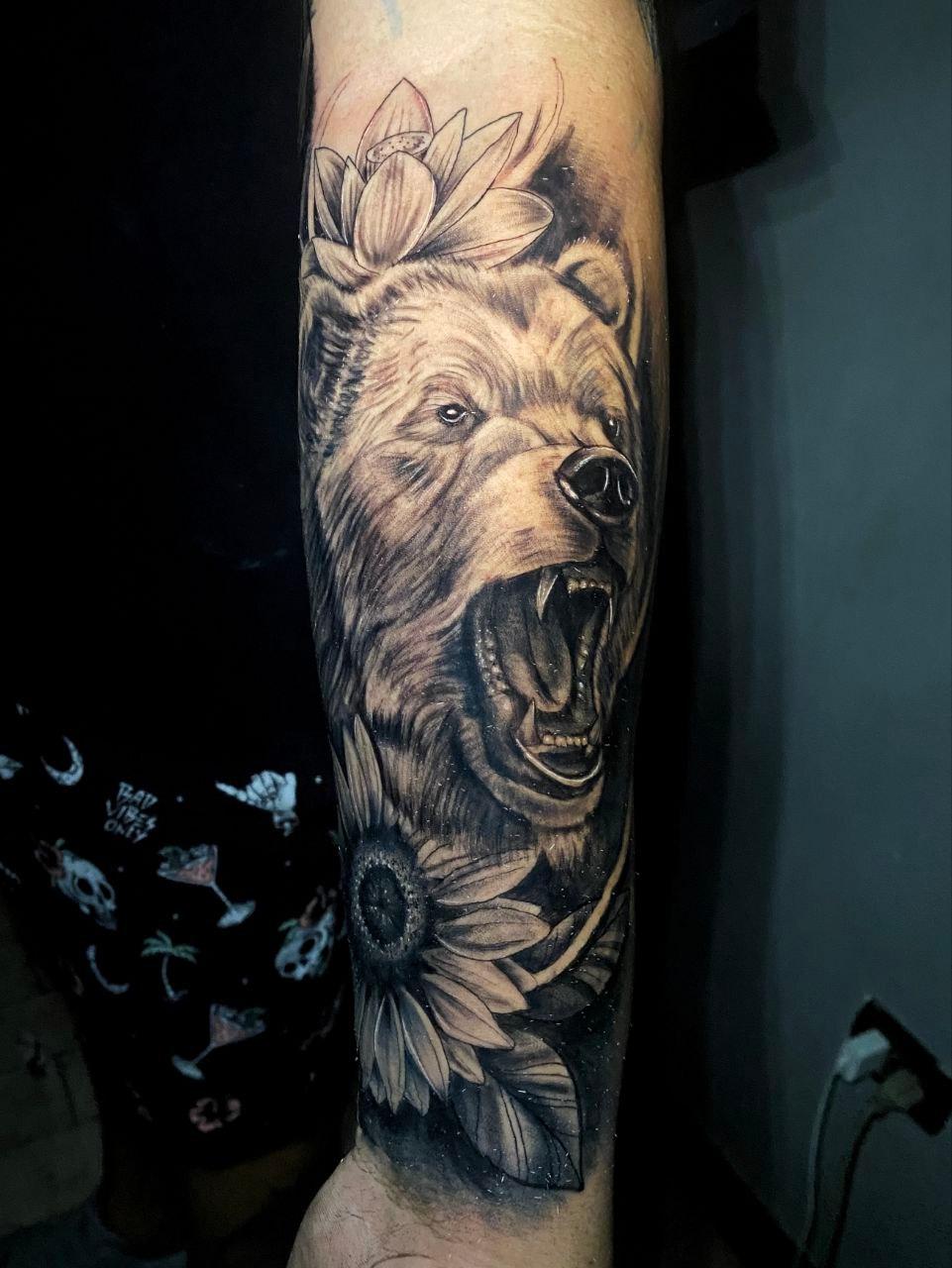 Tatuaje realista de oso con flor de loto y girasol en el brazo