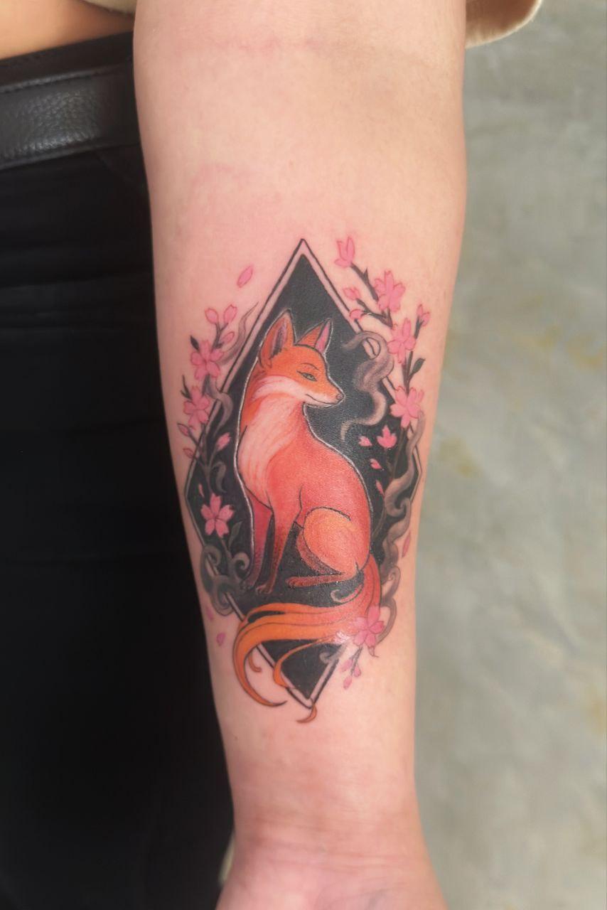 Tatuaje a color de zorro con flores de sakura en el brazo